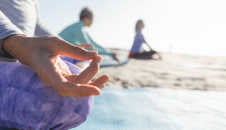 Plusieurs femmes en train de pratiquer le Yoga et la méditation sur une plage lors d'une retraite yoga & méditation à l'École des Secrets